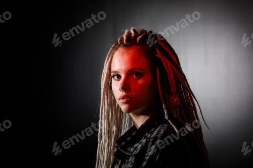 Preview: Portrait Of A Young Woman With Dreadlocks And Piercings In Colored Lighting. Modern Hairstyle Style.