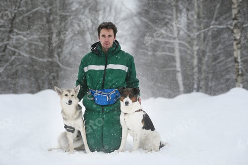 Preview: A Man With Two Cute Middle Size Dogs At Walk Outdoors In Winter. Snow Is Falling