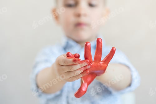 Preview: Cute Boy In A White Shirt On A White Background Looks Outstretched Hands Smeared And Stained With