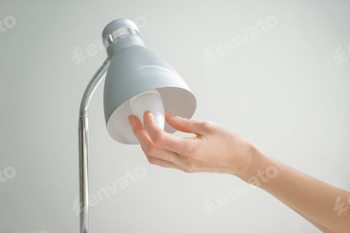 Preview: Woman Changing Light Bulb In Lamp On Grey Background
