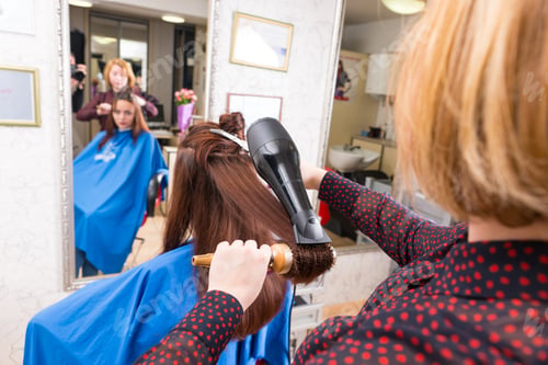 Preview: Rear View Of Young Blond Stylist Drying Hair Of Brunette Client Using Handheld Blow Dryer And Round