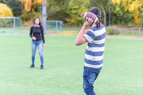 Preview: Back View Of A Male Model Passing American Football To His Female Friend. Couple In Park With