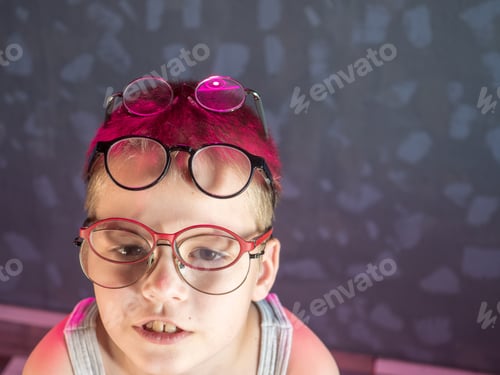 Preview: Photo Of Funny Boy, Blonde Kid With Lot Of Pairs Of Glasses On His Face. Child Is Happy At Home On