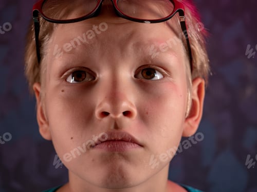 Preview: Cute Blond Child In Blue T-Shirt And Glasses Posing In Front Of Camera And Smiling