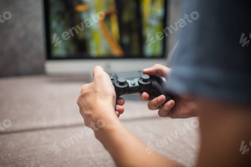 Preview: A Young Man Is Playing With A Joystick On The Game Console On A Background Of A Blurry Monitor