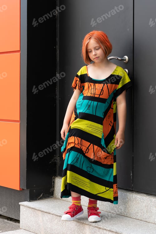 Preview: Little Girl Outside Is Standing Near The House In A Colored Dress