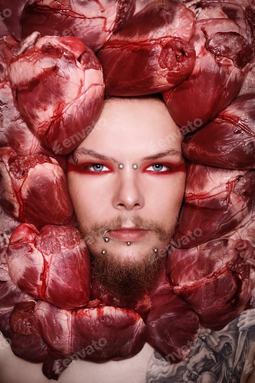 Preview: Conceptual Close-Up Portrait Of Pierced And Tattooed Man With Raw Bloody Hearts Around His Face