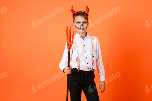 Preview: Halloween Boy With Devil Horns With Pitchforks On Orange Wall Background. High Quality Photo