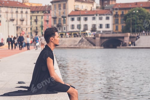 Preview: Young Handsome Asian Model Dressed In Black Tunic Sitting By An Artificial Basin