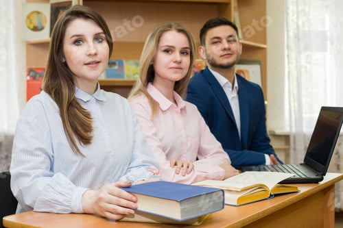 Preview: A Group Of Happy Students With Books Sitting At A Table In The University Library. The Concept Of
