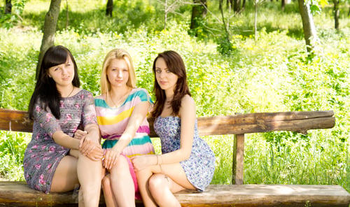 Preview: Three Attractive Young Girls In Stylish Summer Dresses Sitting Close Together On A Wooden Bench In