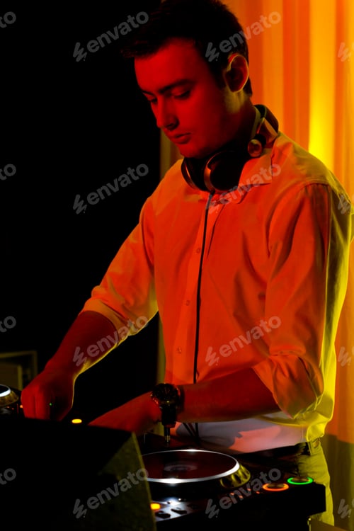 Preview: Disc Jockey Working At His Deck And Turntables Mixing Music In Colourful Party Lighting With A Warm