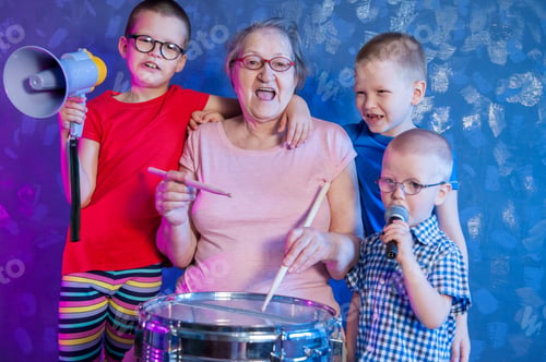 Preview: Elderly Woman In Pink T-Shirt And Glasses Holding Megaphone. Next To Grandmother, Grandchildren In
