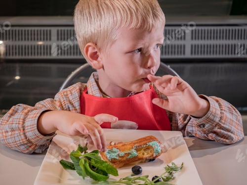 Visualização: Crianças engraçadas em aventais vermelhos comem éclairs cozidos na master class. Educação em confeitaria. Biscoitos