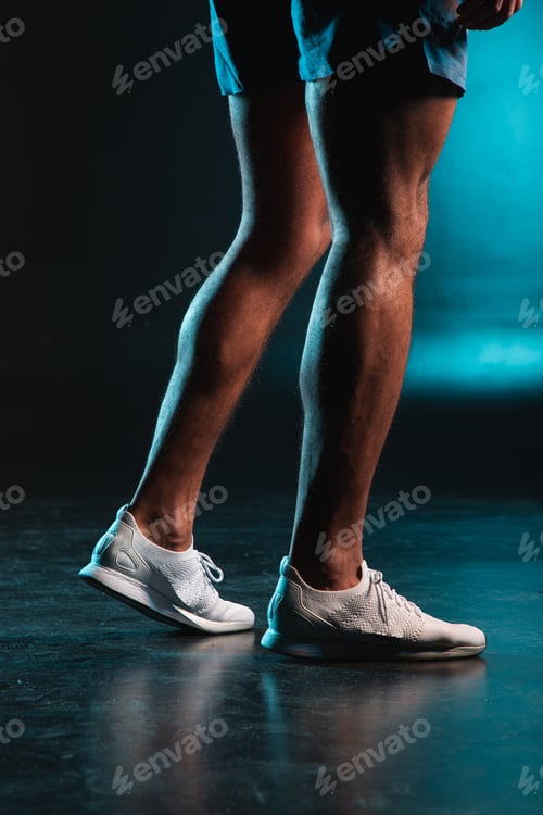 Preview: Cropped Photo Of Legs Of A Sportsman Indoors. Man Standing In Shorts And White Trainers