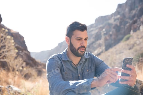 Preview: Man Looking At A Cell Phone And Texting As He Sits In The Mountains