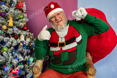 Preview: Elderly Man With Gray Beard And Glasses In Santa Claus Hat With Red Bag Filled With Presents Poses