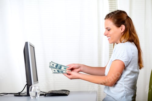 Preview: Portrait Of A Pretty Blonde Woman Holding Plenty Of Cash Money At The Office In Front Computer