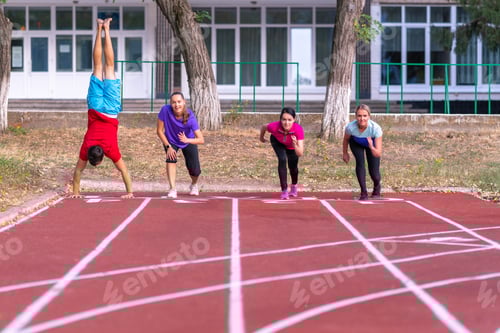 Preview: Young People Lining Up For A Race On A Track As A Friend Practices His Handstands Alongside In A