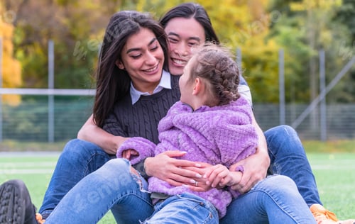 Preview: Happy Mixed Family Hugging In A Park. Parents Hugging Their Autistic Daughter.
