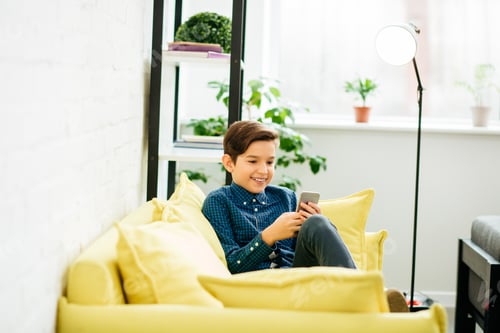 Preview: Boy Sitting with Phone on a Yellow Couch