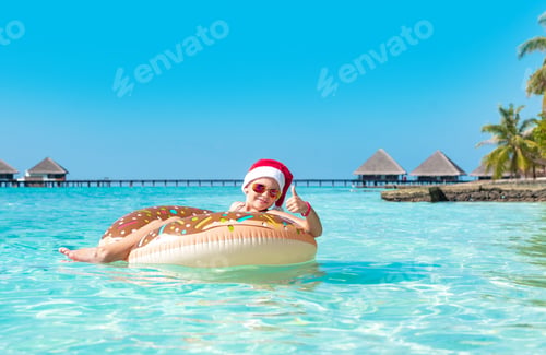 Preview: Cute Boy In A Santa Hat On An Inflatable Donut In The Ocean Having Fun And Gives A Thumbs Up, The