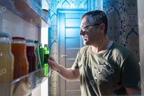Preview: Middle-Aged Casual Man Searching For A Bottle Of Beverage In The Door Of A Fridge With A Point Of