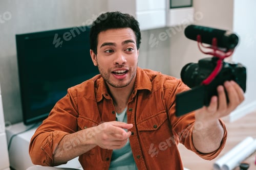 Preview: Confident Attractive Young Man In Shirt And T-Shirt Pointing To The Camera While Recording A Video