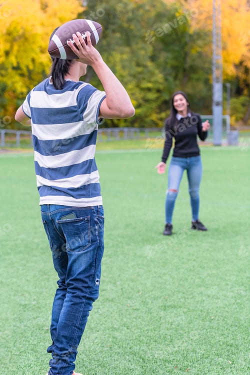 Preview: Back View Of A Male Model Passing American Football To His Female Friend. Couple In Park With