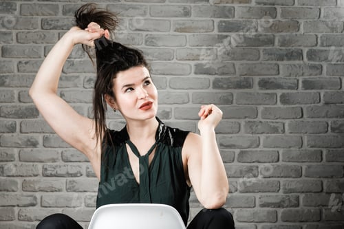 Preview: Woman Styling Hair Indoors Against Gray Brick Wall