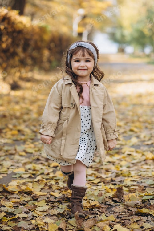 Preview: Happy And Beautiful Little Girl In A Beige Coat Walks In The Autumn Park