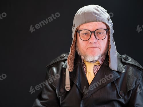 Preview: Elderly Pensioner In Pilot'S Hat, Large Glasses With Gray Beard In Leather Coat Is Looking At