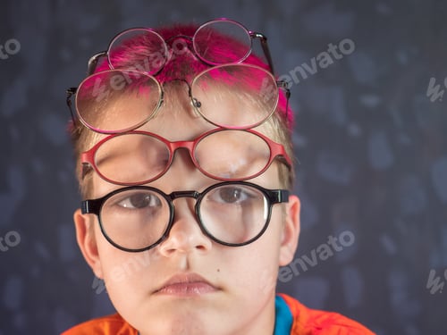 Preview: Photo Of Funny Boy, Blonde Kid With Lot Of Pairs Of Glasses On His Face. Child Is Happy At Home On
