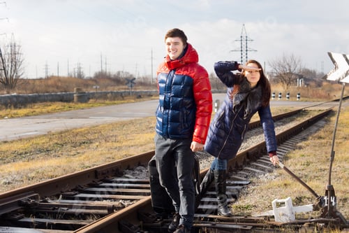 Preview: Playful Couple Waiting For A Train With Luggage Standing Alongside The Track Near A Rural Level