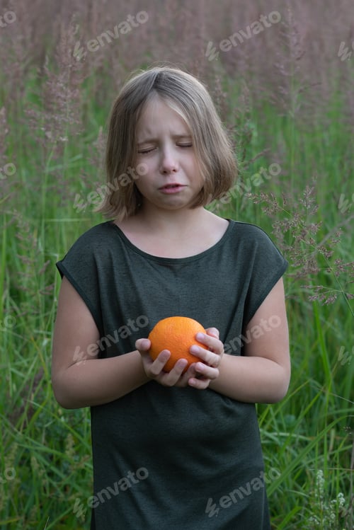 Preview: Little Girl Holds An Orange, Stands Outside In A Green Dress In A Field
