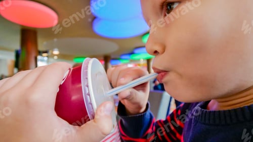 Preview: Cute Little Blond Child Drinks Carbonated Drink And Eats Burger In Fast Food Cafe. Concept Of Fast