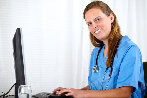 Preview: Portrait Of A Beautiful Friendly Nurse Smiling While Working On Computer At Workplace