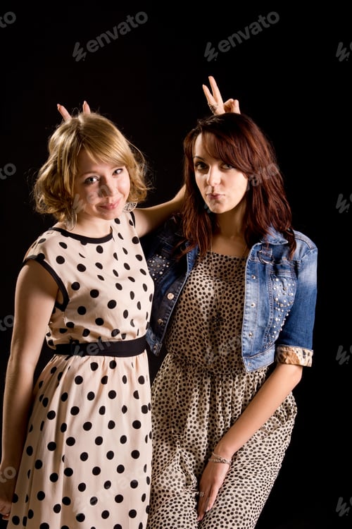 Preview: Playful Attractive Young Girls Standing Side By Side Making V-Signs Behind Each Others Heads While
