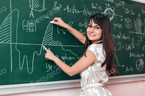 Preview: Teacher Write An Example On The Blackboard And Explain A Lesson Looking At The Camera.Concept