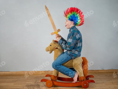 Preview: Happy Boy In Plaid Shirt Is Rolling On Rocking Horse Toy. Baby With Wonderful Punk-Style Colored