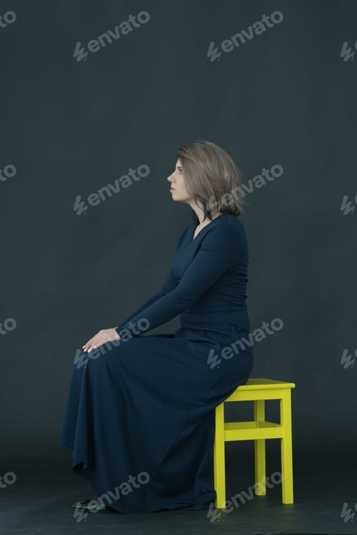Preview: Young Beautiful Girl Posing In Studio In Dress Sitting On Chair On Dark Background