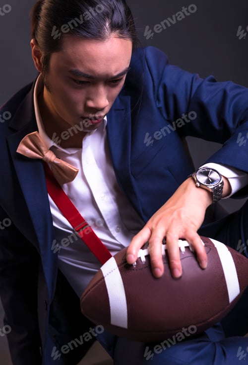 Preview: Asian Male Model Holding Ball For American Football Isolated On Dark Background