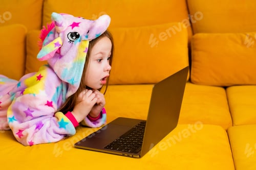 Preview: Little Girl In Kigurumi Lies At Home On A Couch With A Laptop. Children'S Distance Education