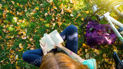 Preview: Girl In The Park Sits Under A Tree And Reads A Book. Next To It There Is A Bicycle And A Backpack