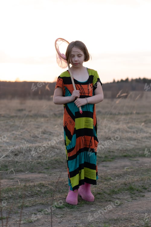 Preview: Little Scandinavian Girl In A Field In Spring With A Net Stands In A Colored Dress
