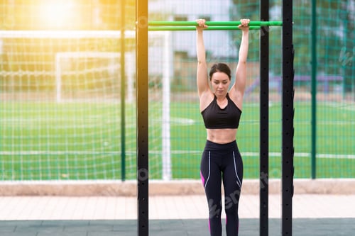 Preview: Fit Toned Young Woman Athlete Working Out On Parallel Bars At An Outdoor Gym Backlit By The Warm