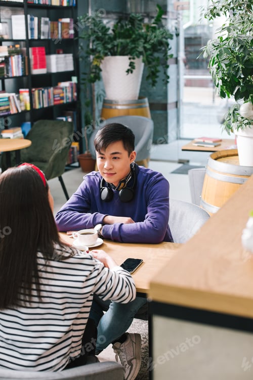 Preview: Young Asian Man Sitting Opposite The Long Haired Lady At The Table With A Cup Of Coffee In Front Of