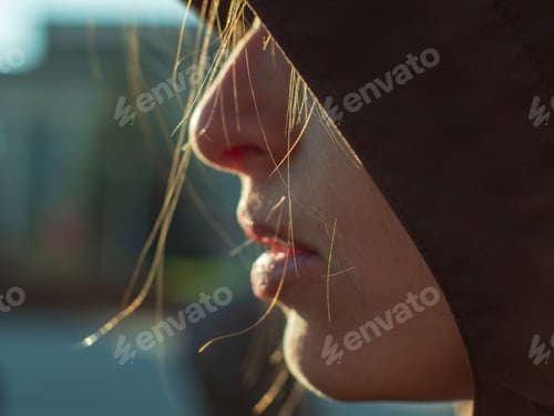 Preview: Young Woman With Beautiful Face In Dark Hood Poses In Front Of Camera In Front Of Sunlight. Thin