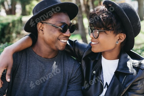 Preview: Stylish Young African Couple In Sunglasses Speaking And Sitting In The Park Of Summer