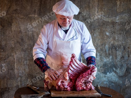 Preview: Elderly Man With A Gray Beard In Cook Suit And White Apron Cuts Into Pieces Large Piece Of Pork